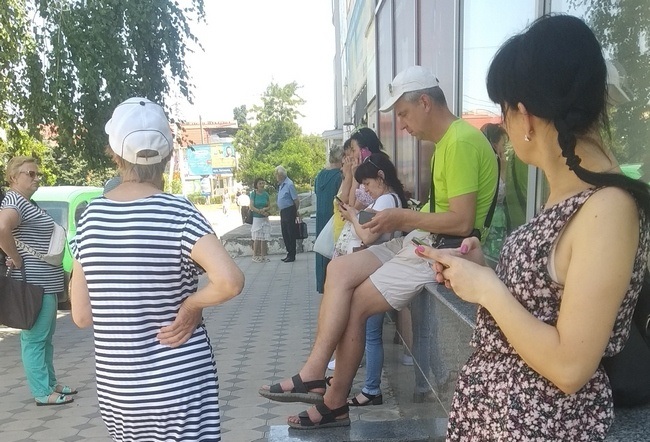 Жителі Нової Каховки ловлять інтернет біля будівлі City Center. Червень 2022 року