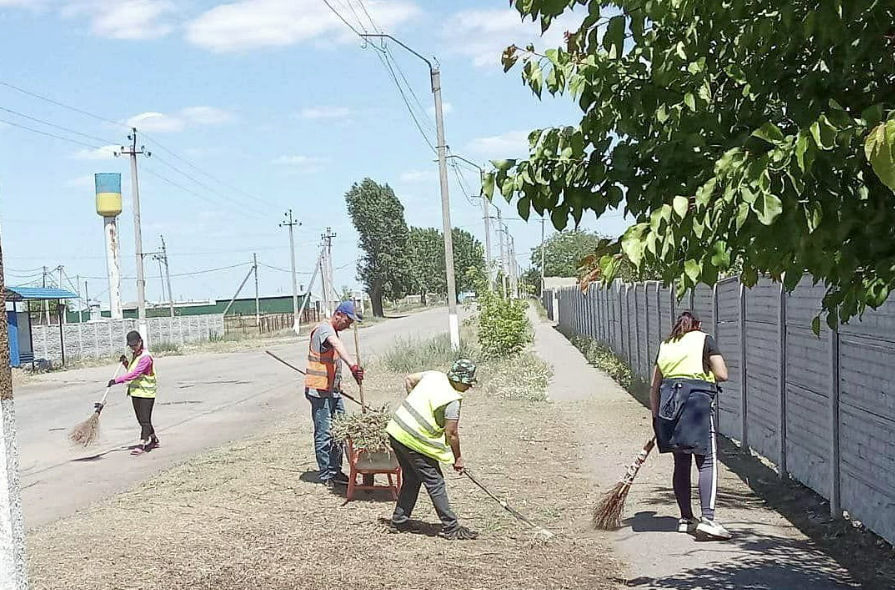 Комунальники у Новокаховській громади прибирають вулиці. На задньому плані - водонапірна башта в кольорах прапора України