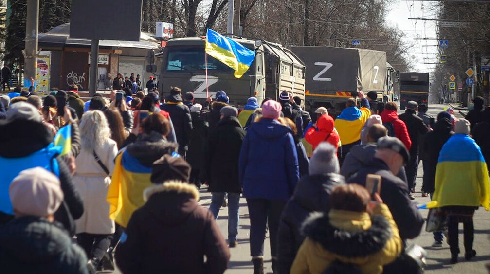Люди з українськими прапорами йдуть до вантажівок російської армії під час мітингу проти російської окупації в Херсоні, 20 березня 2022 р.